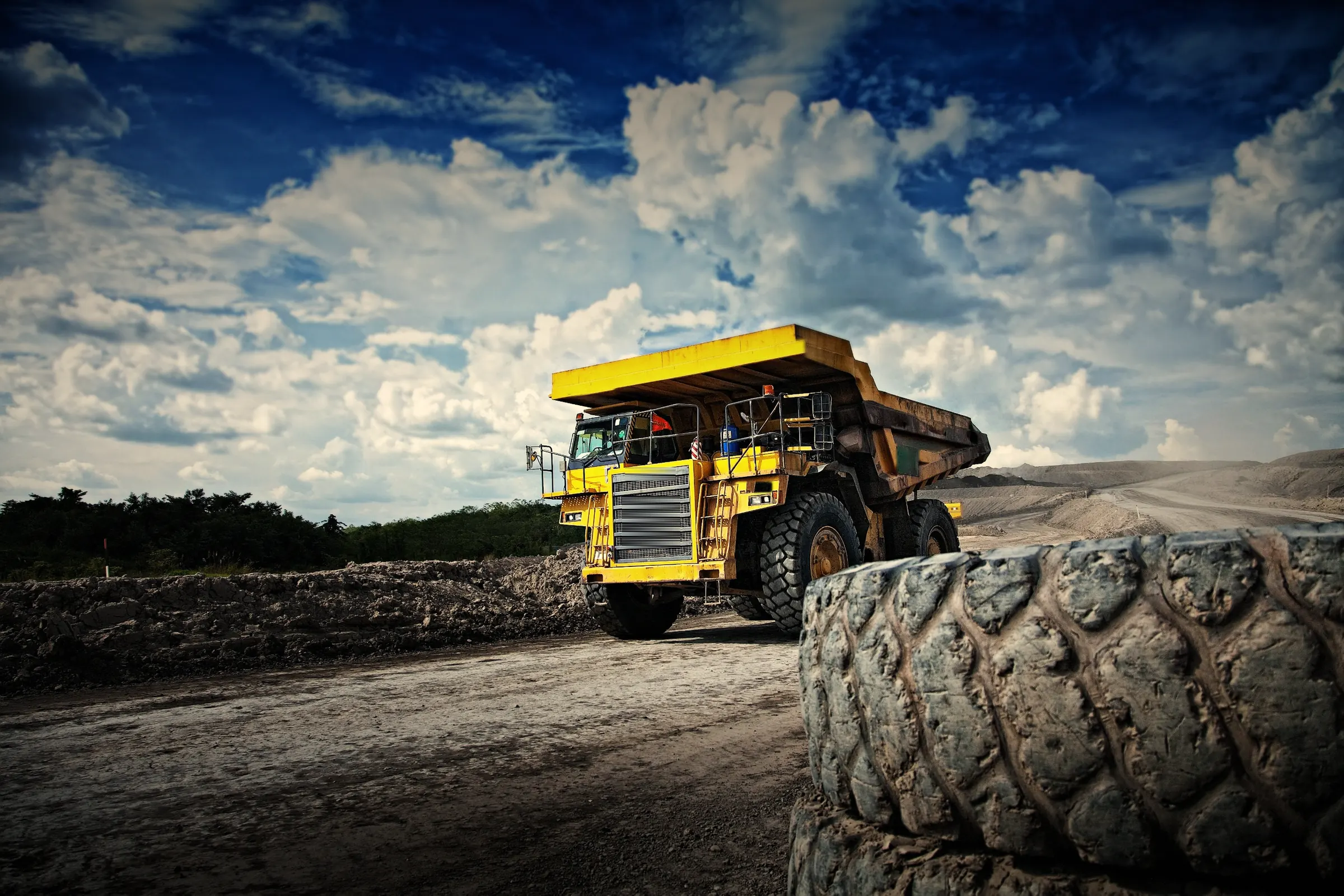 Rigid haul truck on a coal-mine haul road, with a giant OTR tyre in the foreground